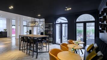 Un interior moderno con suelo de parqué tipo espiga, una zona de comedor central con una mesa larga y sillas, y un área de descanso con mesas redondas y sofás.