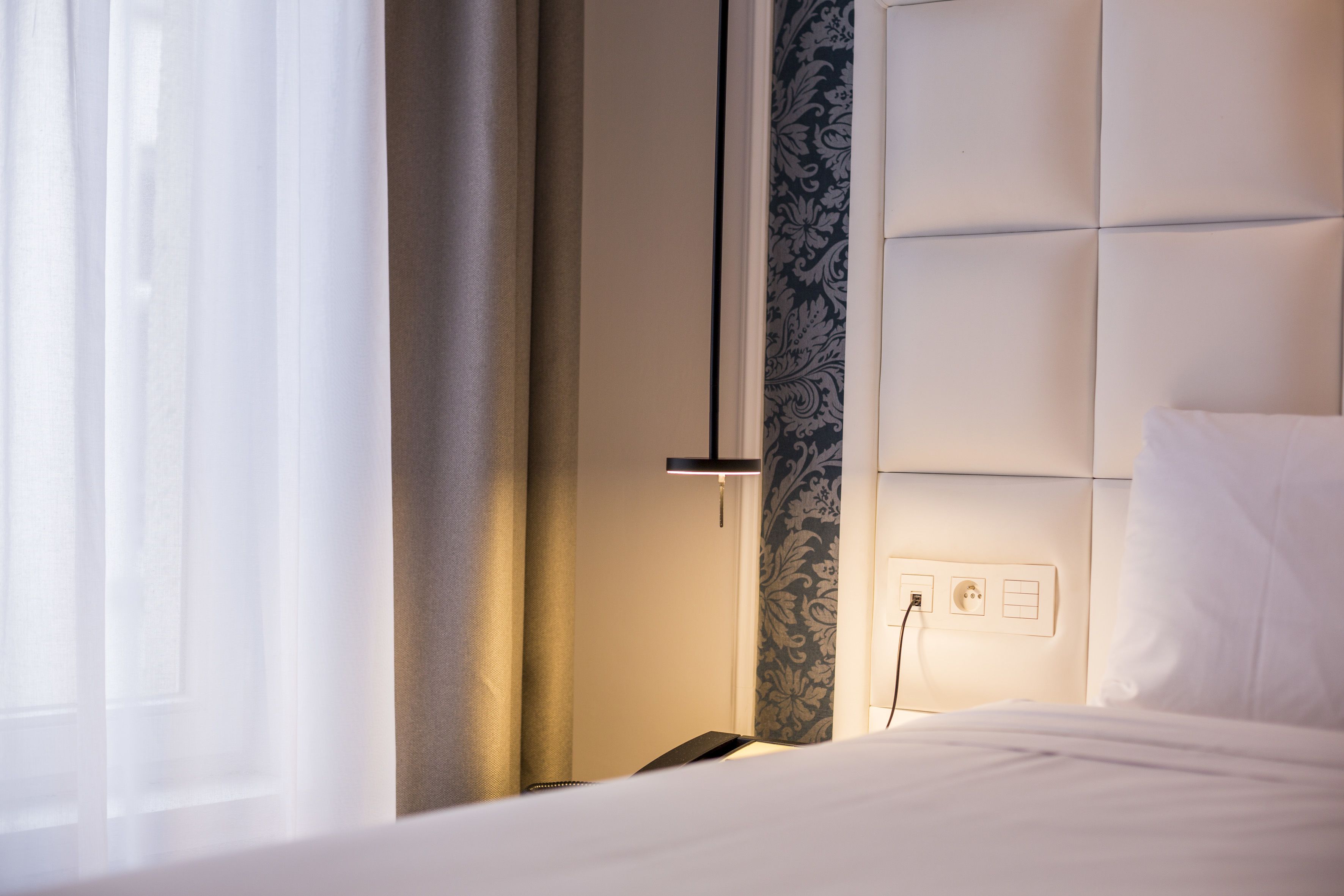 Ein Hotelzimmer mit Bett, Nachttisch, Lampe und Steckdose an der Wand.