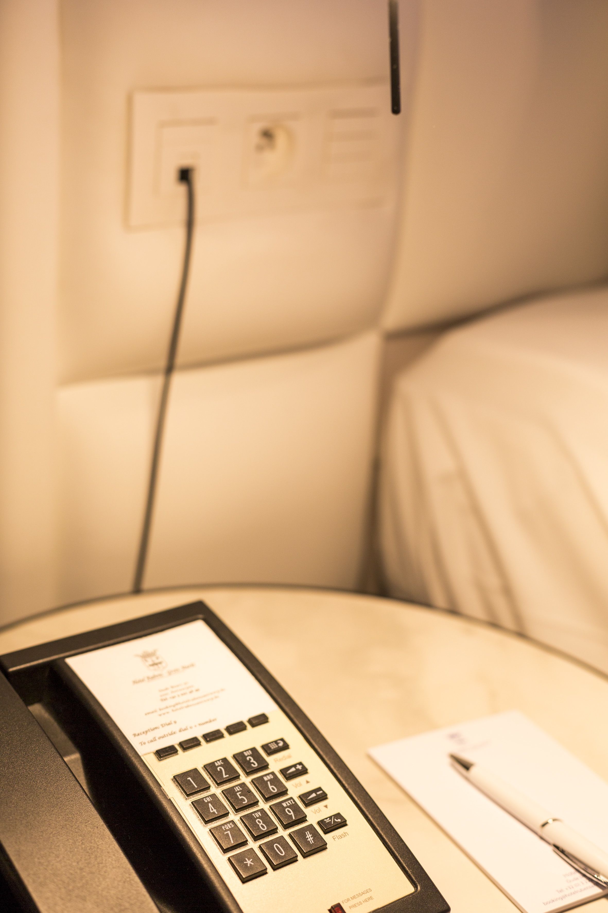 Una habitación de hotel con un teléfono, un bolígrafo y un papel sobre una mesita de noche.