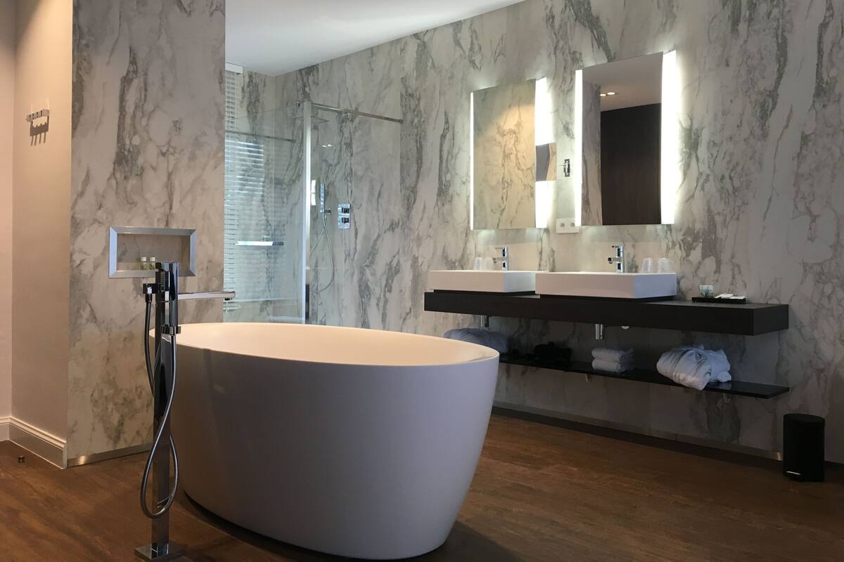 Een moderne badkamer met een vrijstaand bad, een douche met glazen wanden en een grote spiegel boven een tweepersoons wastafel.