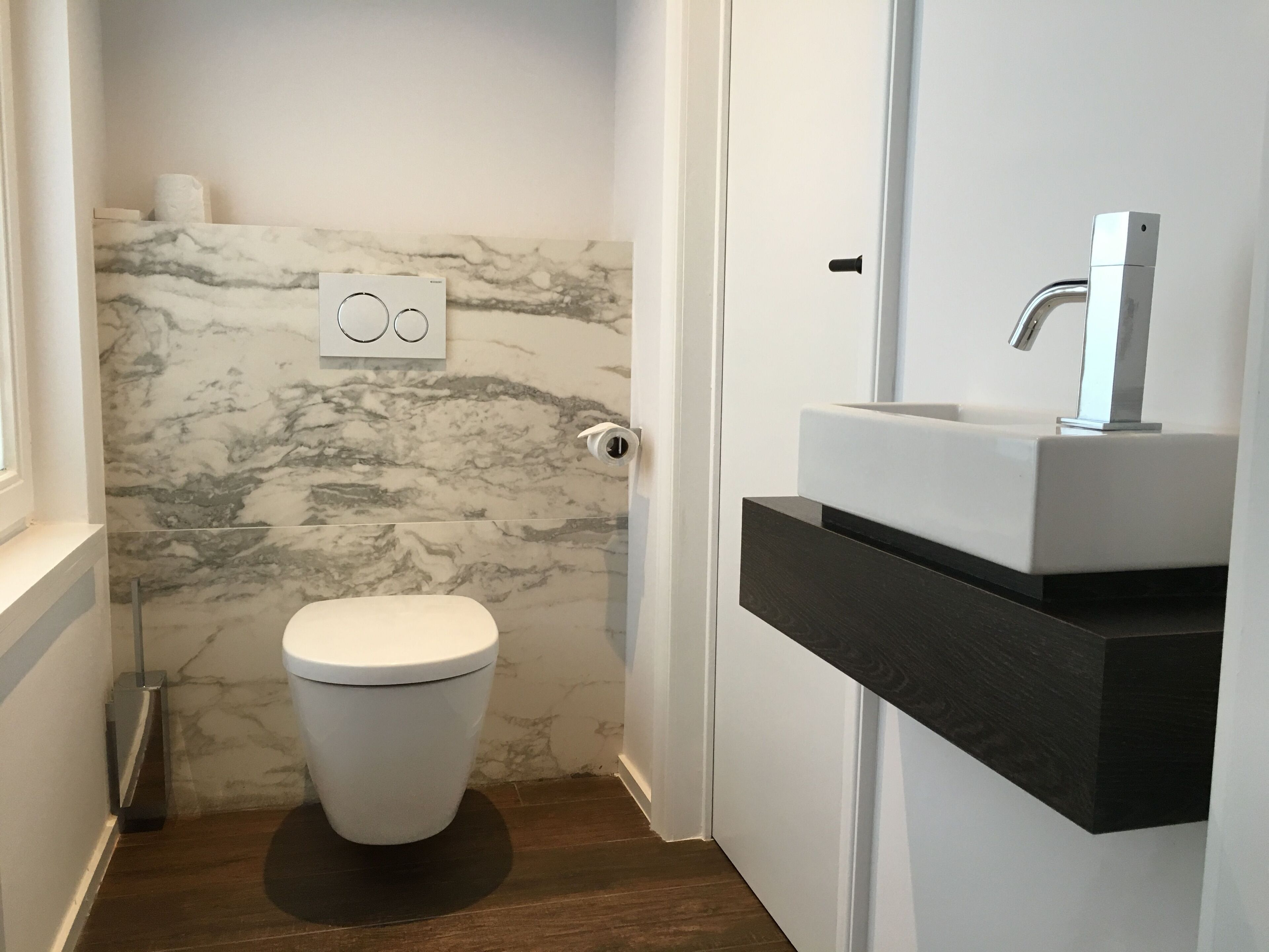 A modern bathroom with a toilet, marble wall, and a sink with a mirror.