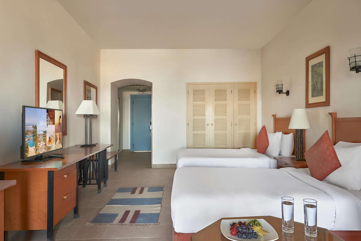 Una habitación de hotel con una cama, mesitas de noche, un escritorio, un televisor y una puerta que da a otra estancia.