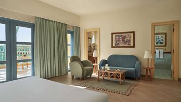 Habitación de hotel con cama, sofá azul, sillón verde, una mesita con lámpara y vista a un edificio a través de la ventana.