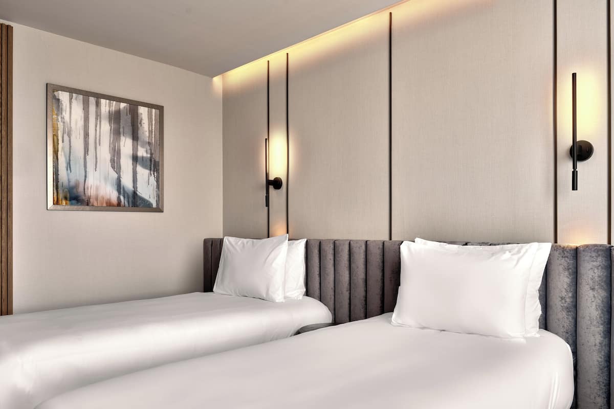 A hotel room with two beds, a large abstract painting on the wall, and a modern light fixture.