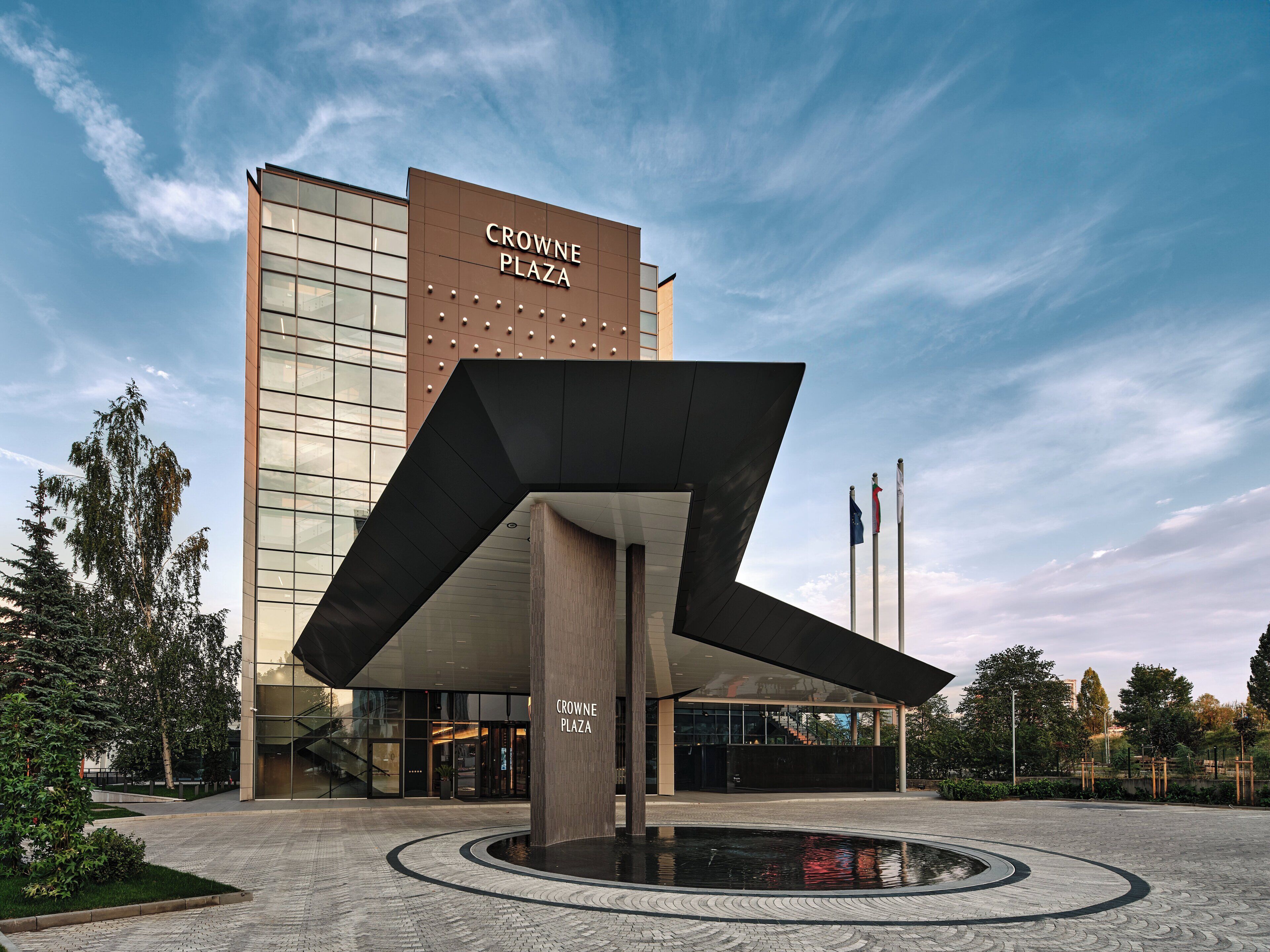Een modern gebouw met het bord "CROWNE PLAZA" en een unieke geometrische sculptuur ervoor.