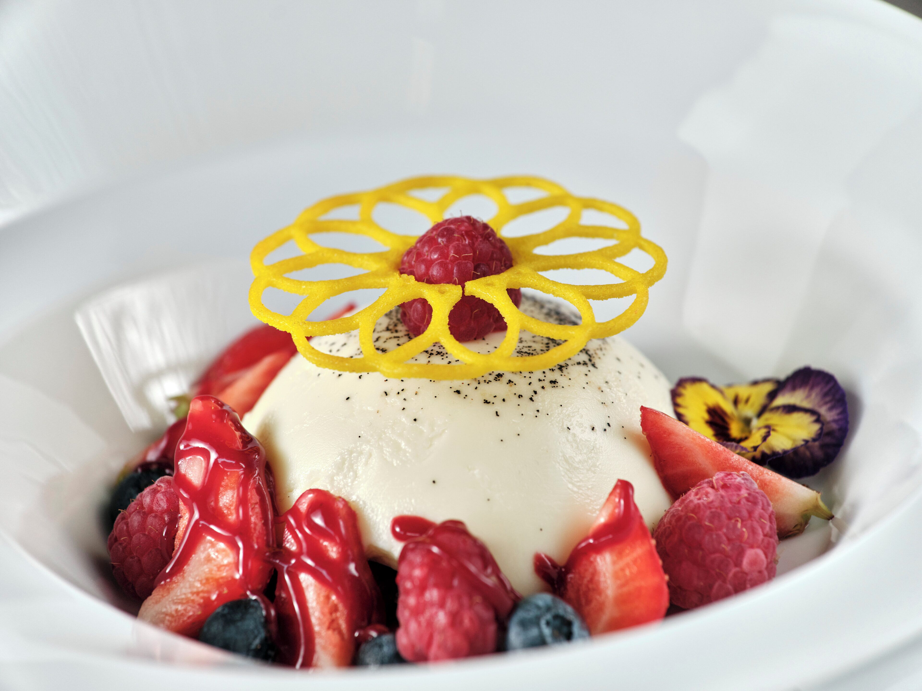 A dessert with a yellow decorative piece on top, surrounded by strawberries and raspberries.