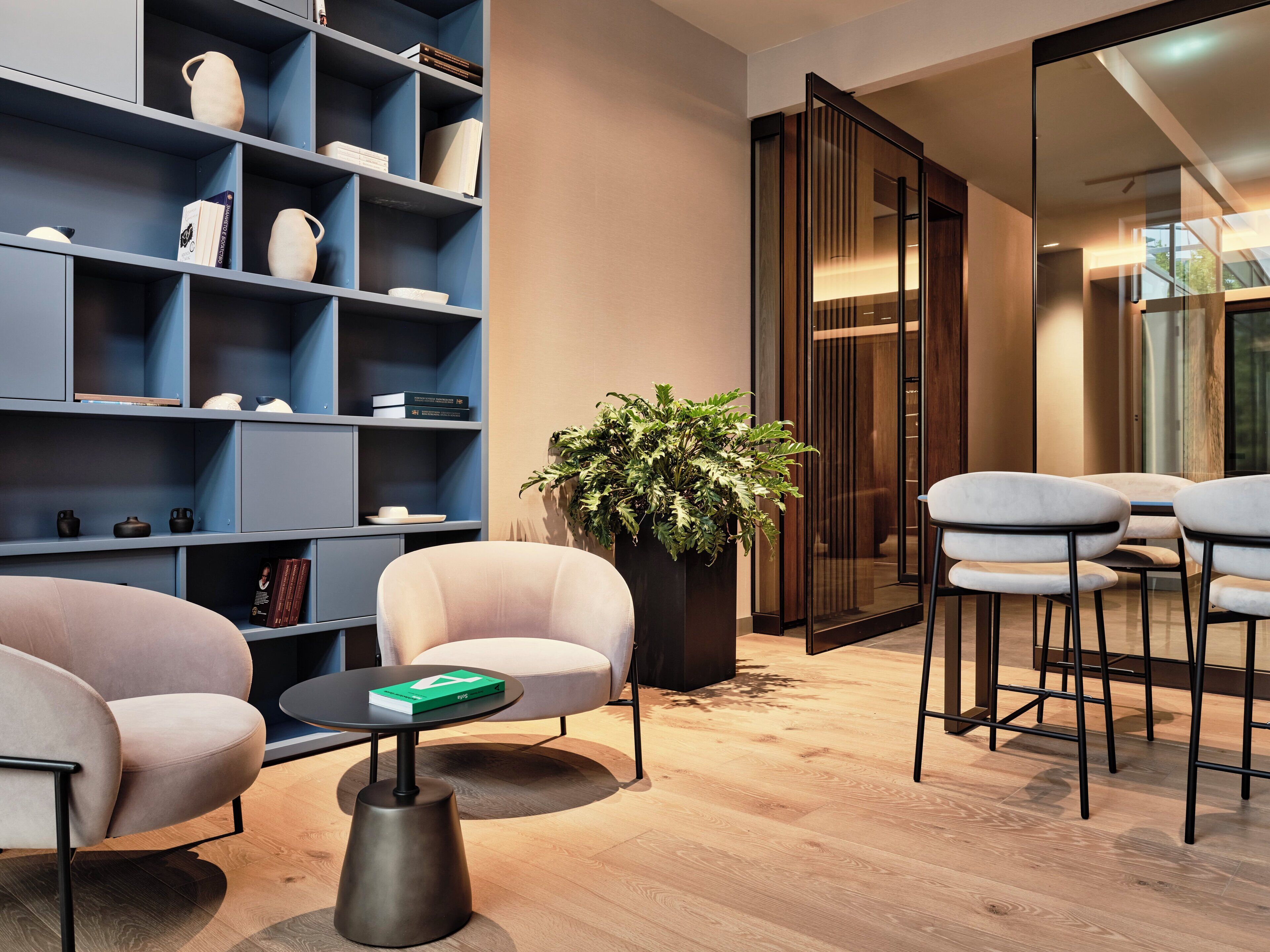 Una sala de estar moderna con una estantería azul, una planta grande en maceta y un área de descanso con dos sillones y una mesa de centro.