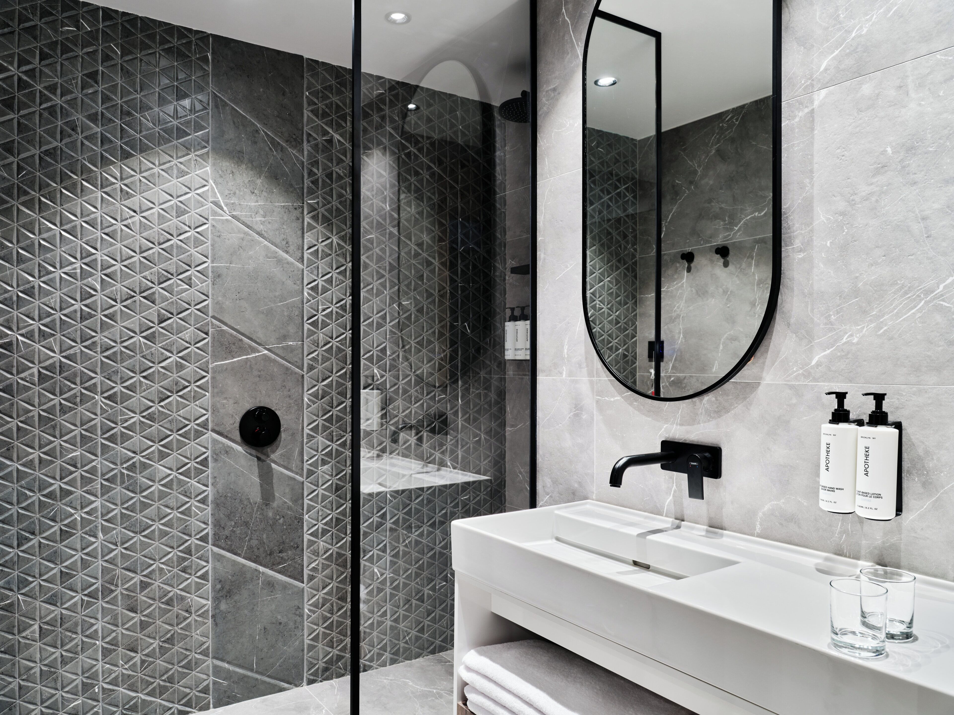 A modern bathroom with a large mirror, a white sink, and a shower area.