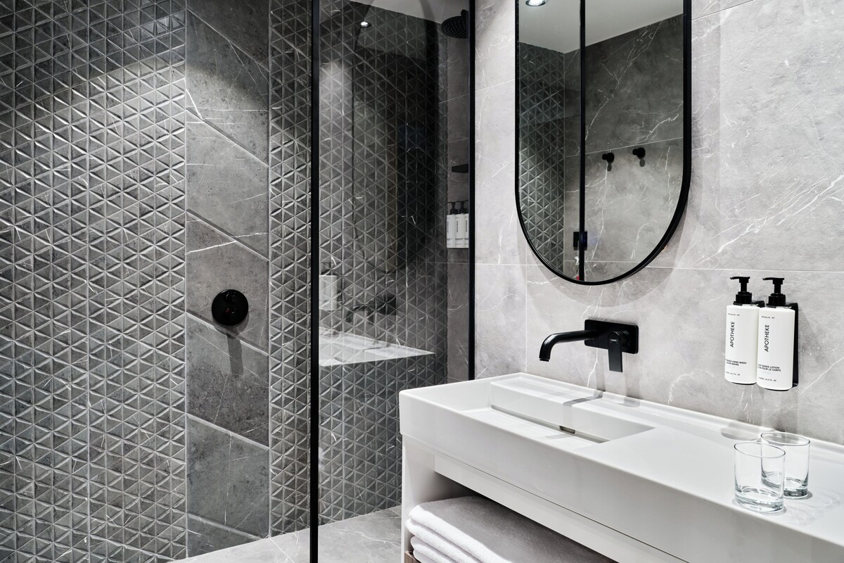A modern bathroom with a large mirror, a white sink, and a shower area.