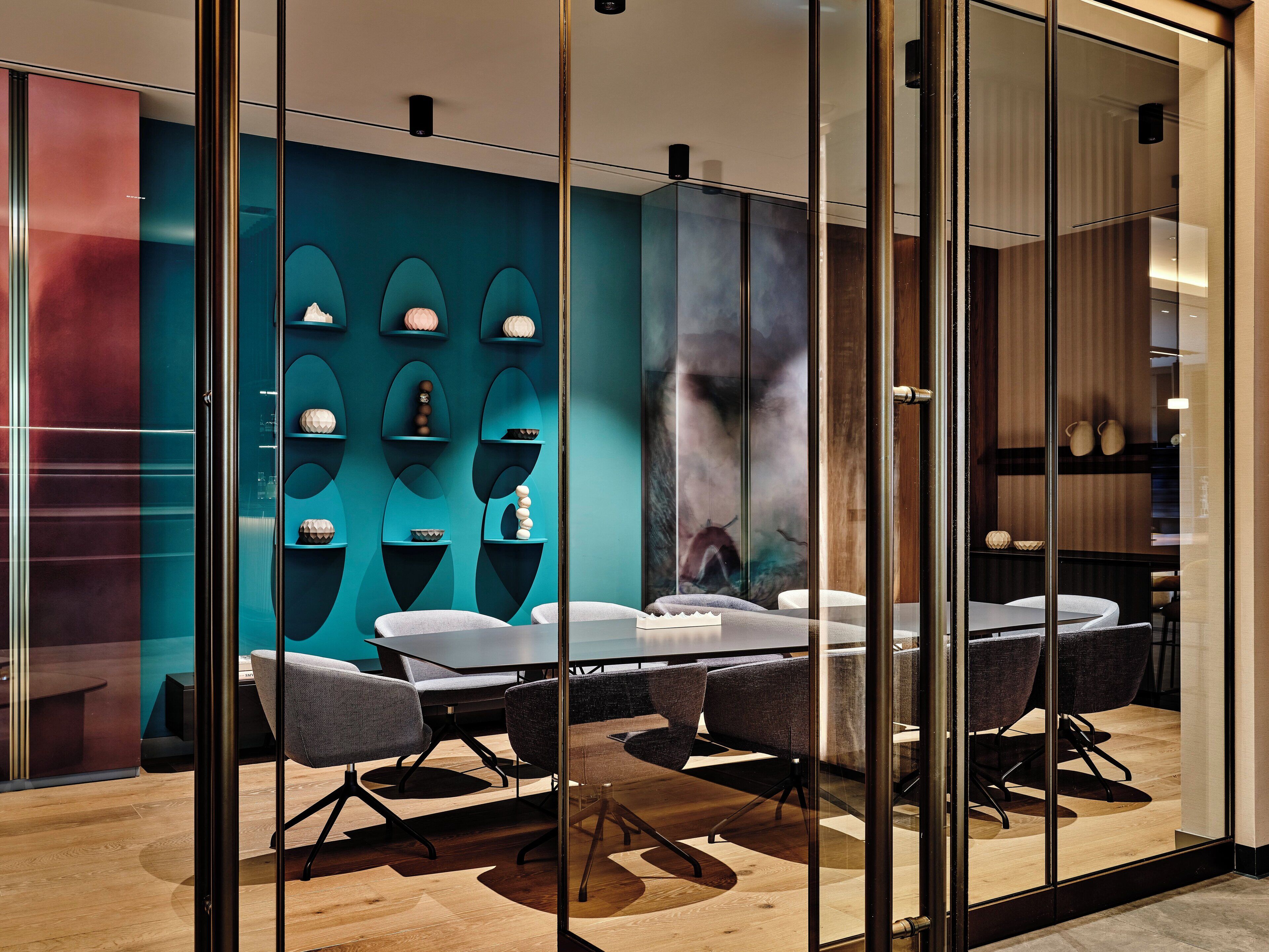 A modern conference room with a glass partition, a wooden table, and grey chairs.