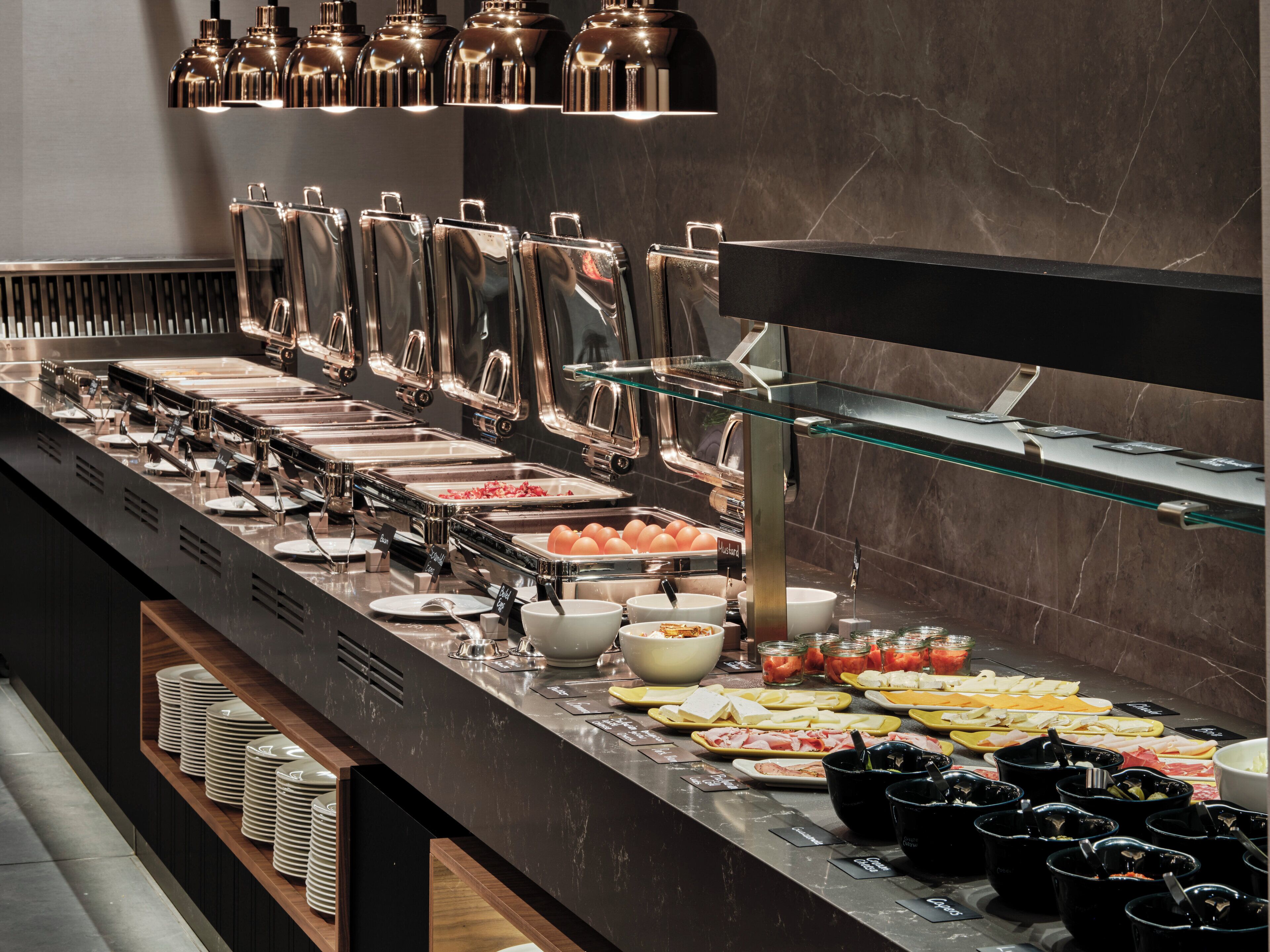 A buffet with various food stations, including a salad bar, hot dishes, and a cheese station.