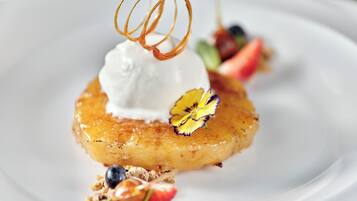 Postre sobre un plato blanco con una bola de helado, una base de fruta caramelizada y adornos que incluyen una flor y frutos rojos.