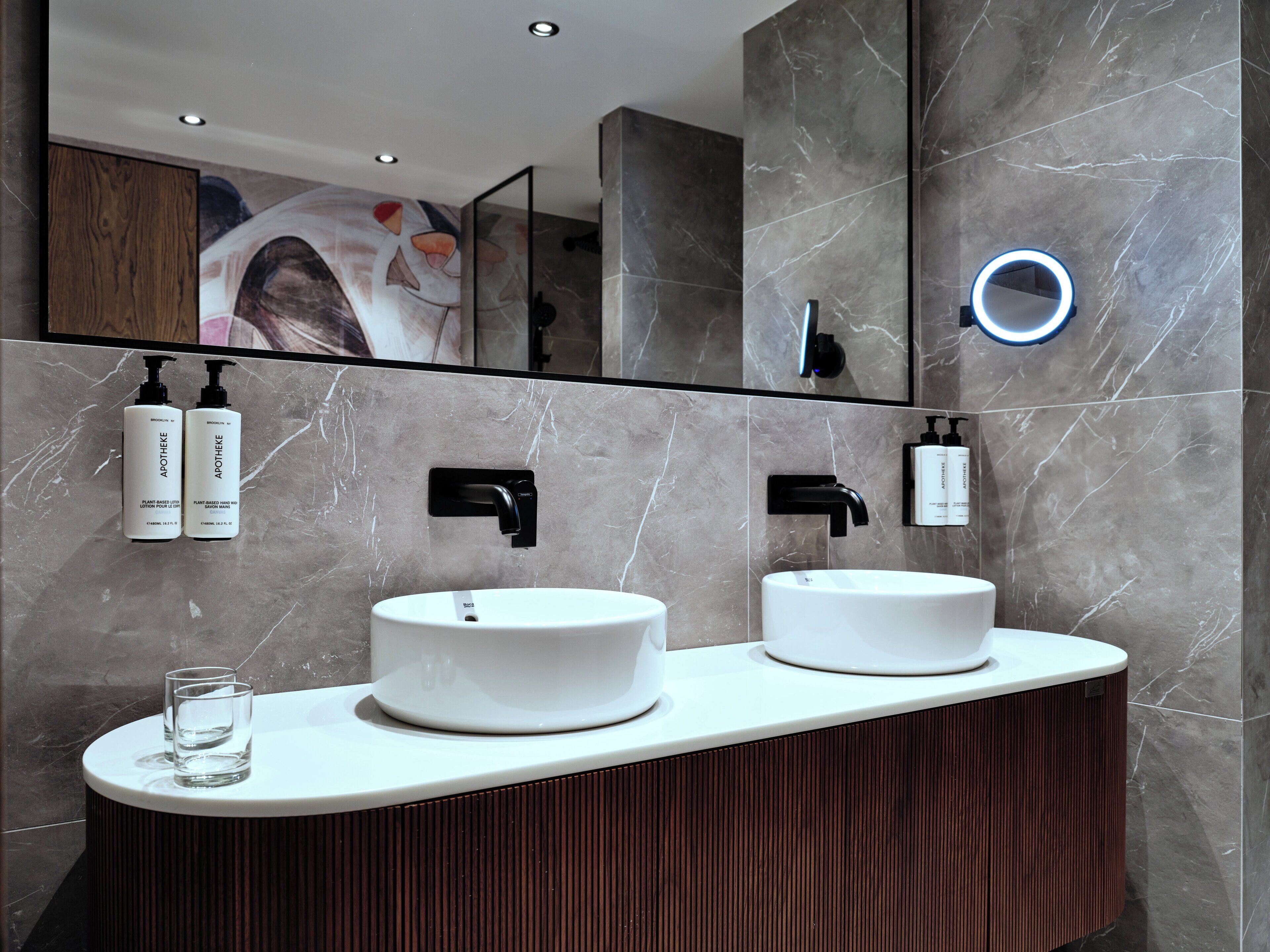 A modern bathroom with two sinks, a mirror, and a ring light.