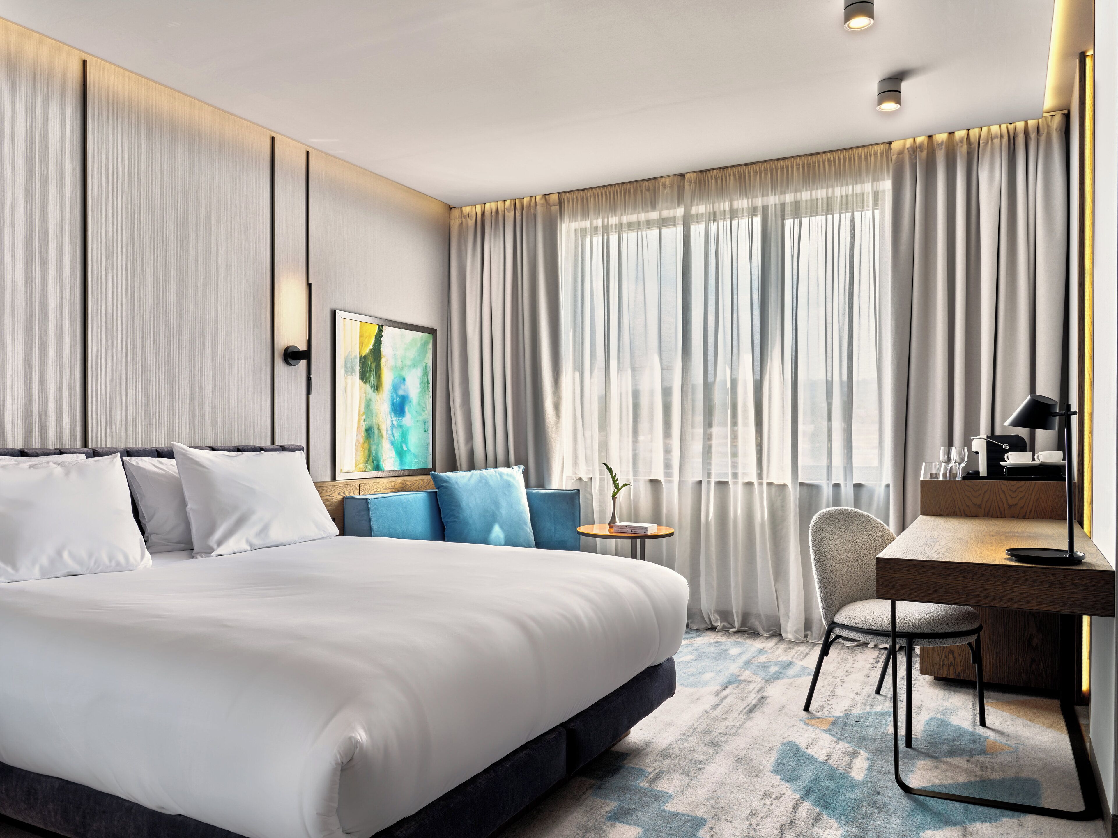 Ein modernes Hotelzimmer mit einem großen Bett, einem Schreibtisch und einem Sessel.