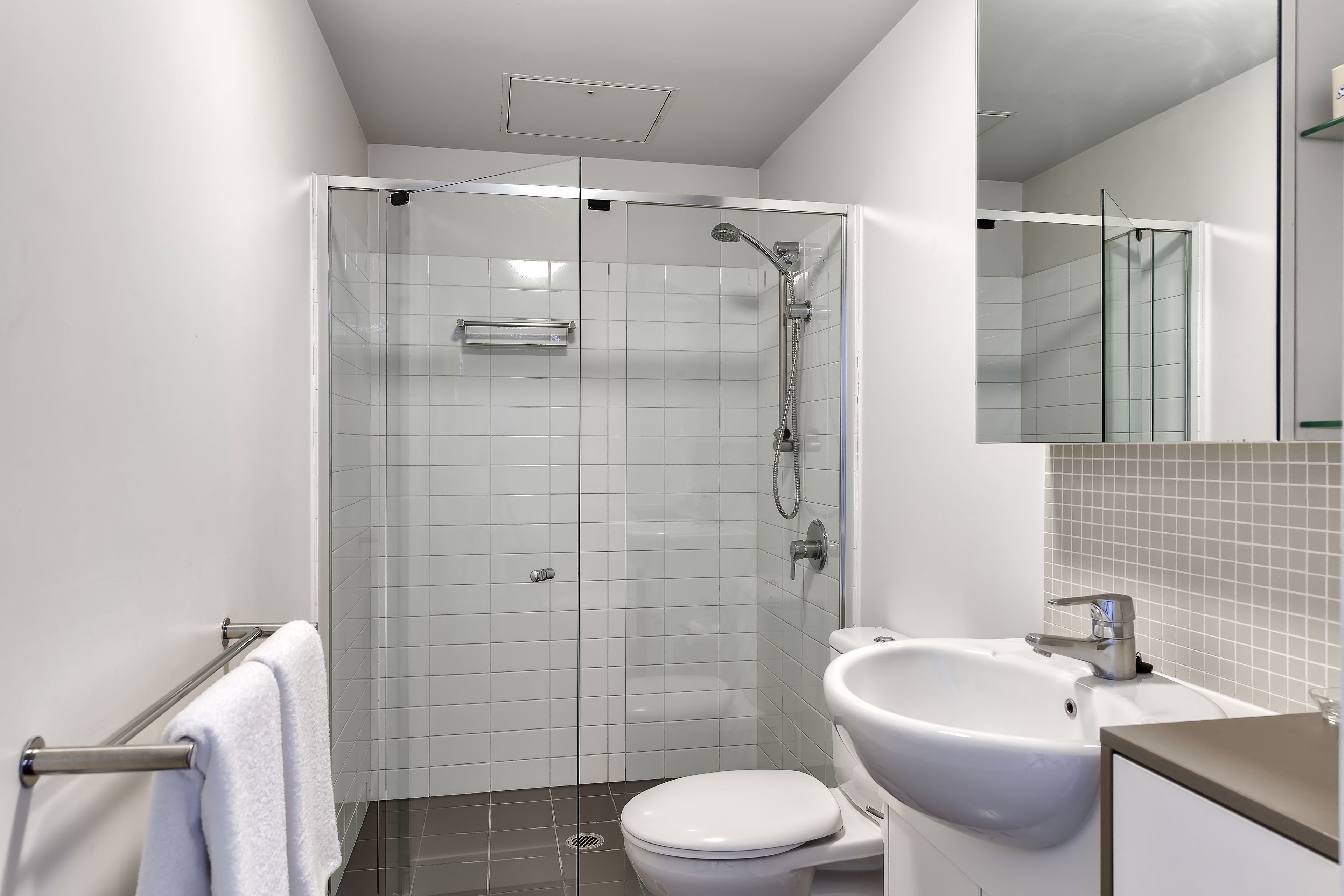 Un baño moderno con ducha de vidrio, inodoro blanco y lavamanos con espejo.