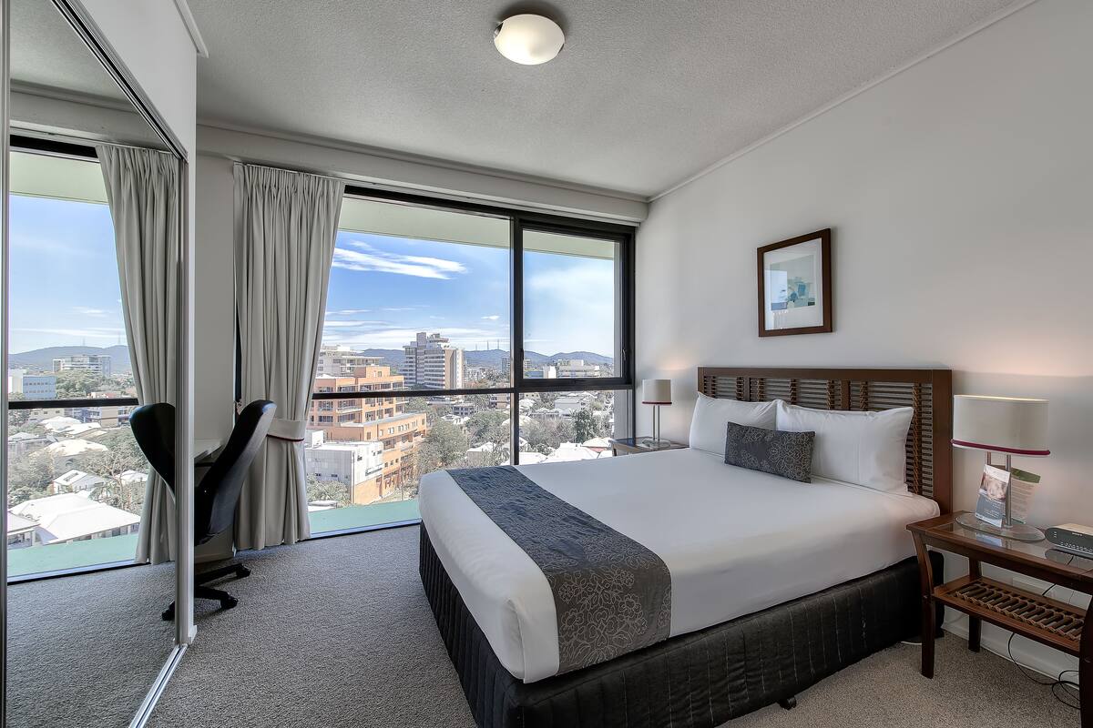A hotel room with a large bed, a desk, a chair, and a view of the city.