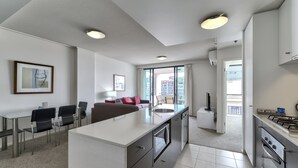 A modern kitchen with a central island, a dining area with chairs, and a view of the outside balcony. - SKD SUITES (Spring Hill)