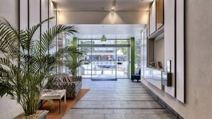 A modern hotel lobby with a tiled floor, a reception desk, a patterned sofa, and potted plants. - SKD SUITES (Spring Hill)