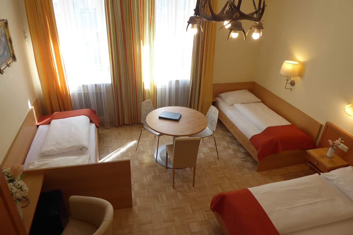Ein Hotelzimmer mit zwei Einzelbetten, einem kleinen runden Tisch mit einem Stuhl, einem Holzstuhl und einem Nachttisch mit Lampe.