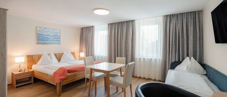 Ein Hotelzimmer mit einem Bett, einem Schreibtisch, zwei Stühlen, einem kleinen Tisch, einem Nachttisch, einer Lampe und einem Bild an der Wand.