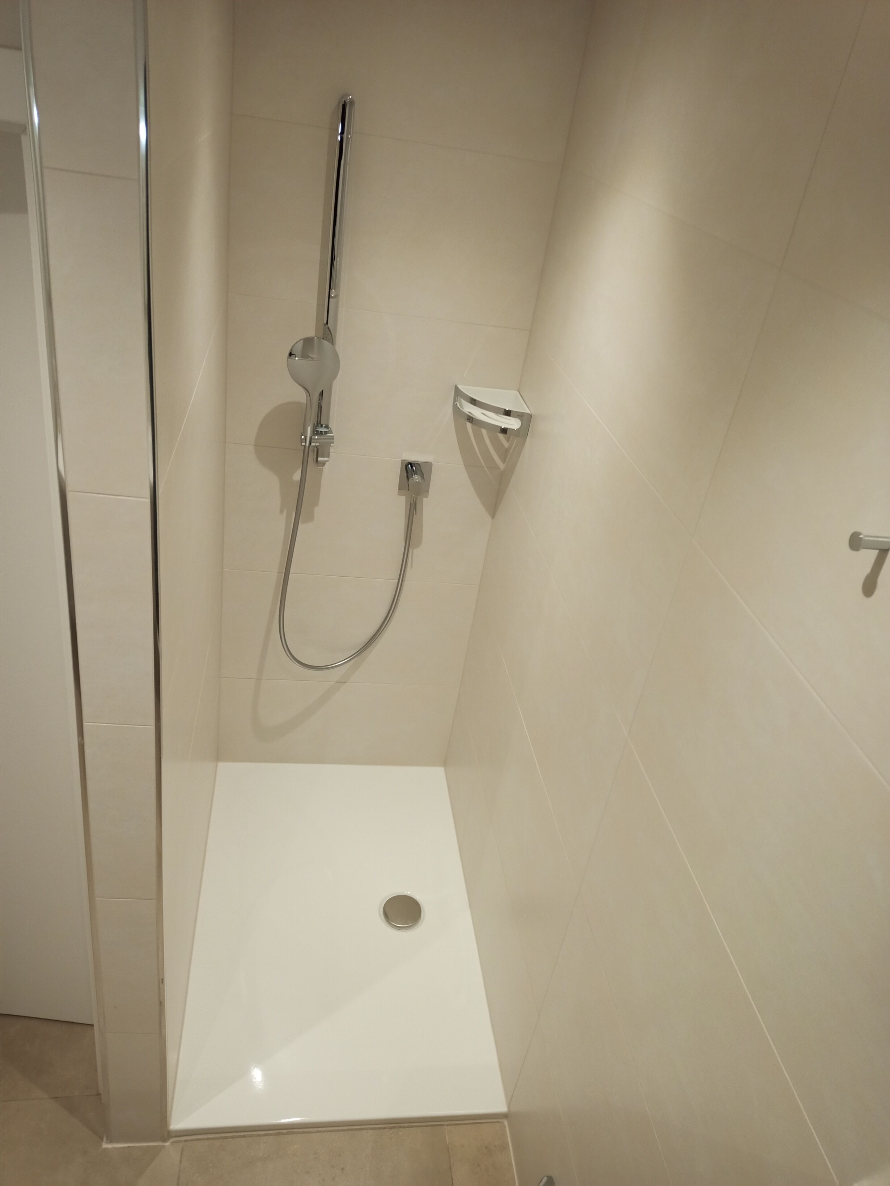 Pequeño espacio de ducha moderno con mampara de vidrio, cabezal de ducha de mano y grifo empotrado.