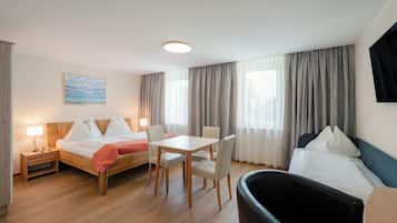 A hotel room with a bed, a desk, two chairs, a small table, a nightstand, a lamp, and a painting on the wall.
