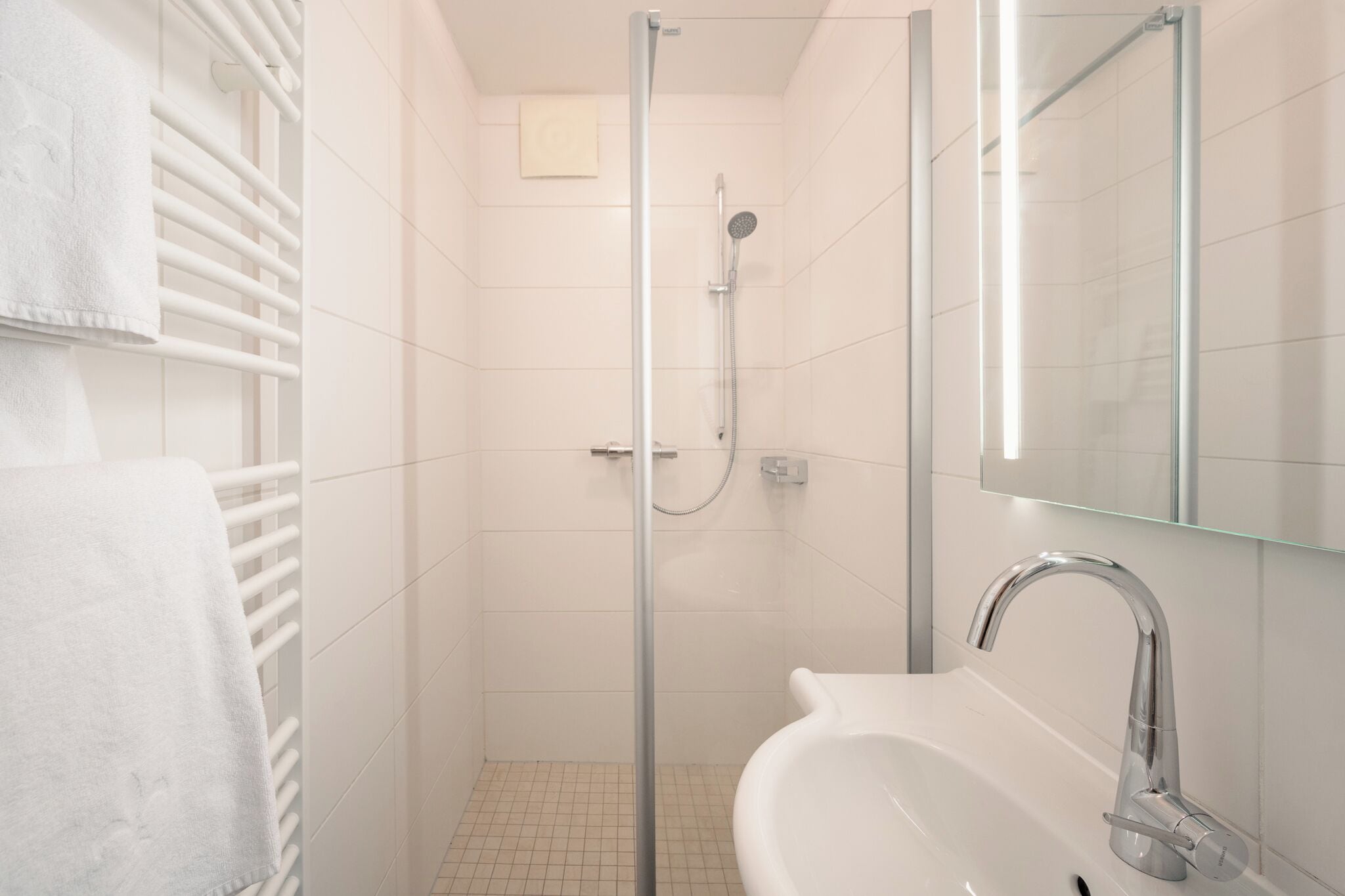 A modern bathroom with a glass shower enclosure, a white sink, and a towel rack.