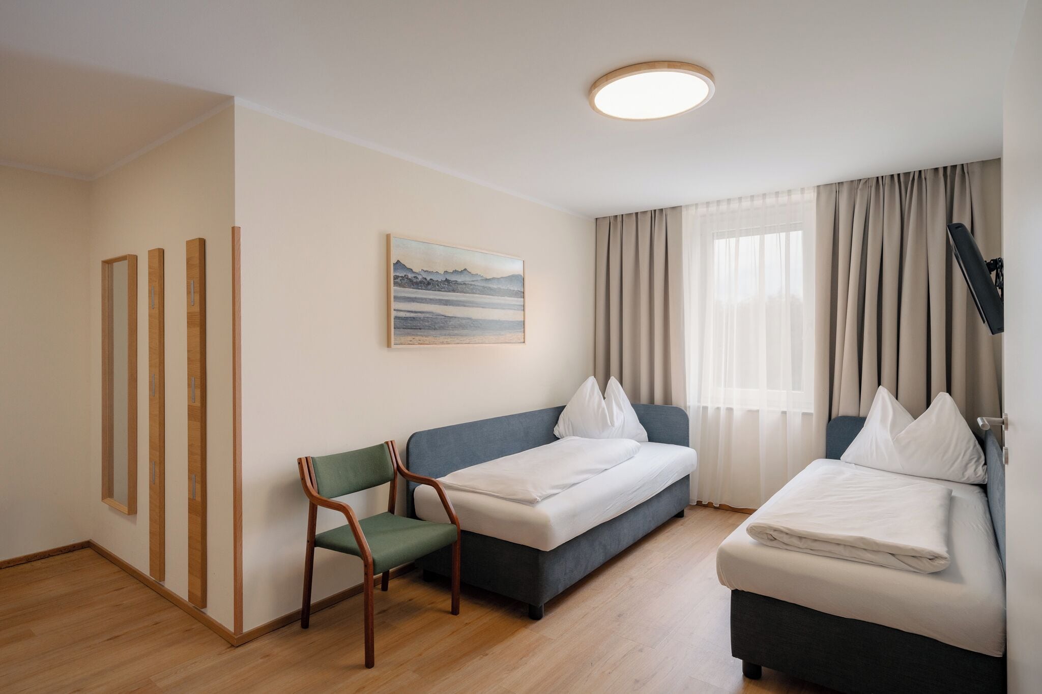 Ein Hotelzimmer mit einem Bett, einer Couch, einem Sessel, einem Gemälde und einem Fenster mit Vorhängen.