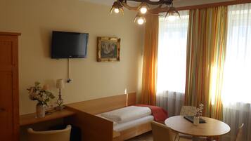 A hotel room with a bed, a desk, a chair, a table, a TV, and a chandelier.