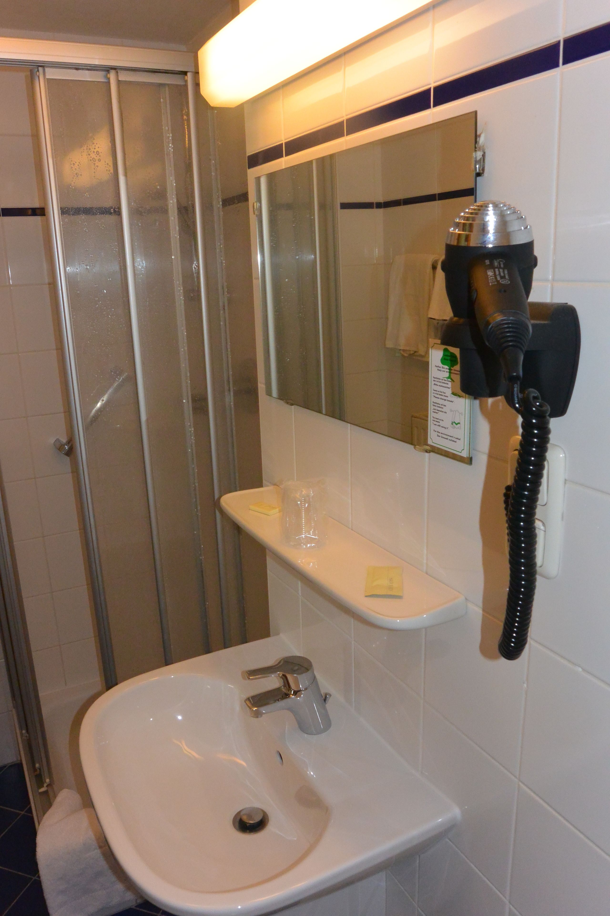 A bathroom with a glass shower enclosure, a white sink with a mirror above it, and a hairdryer mounted on the wall.