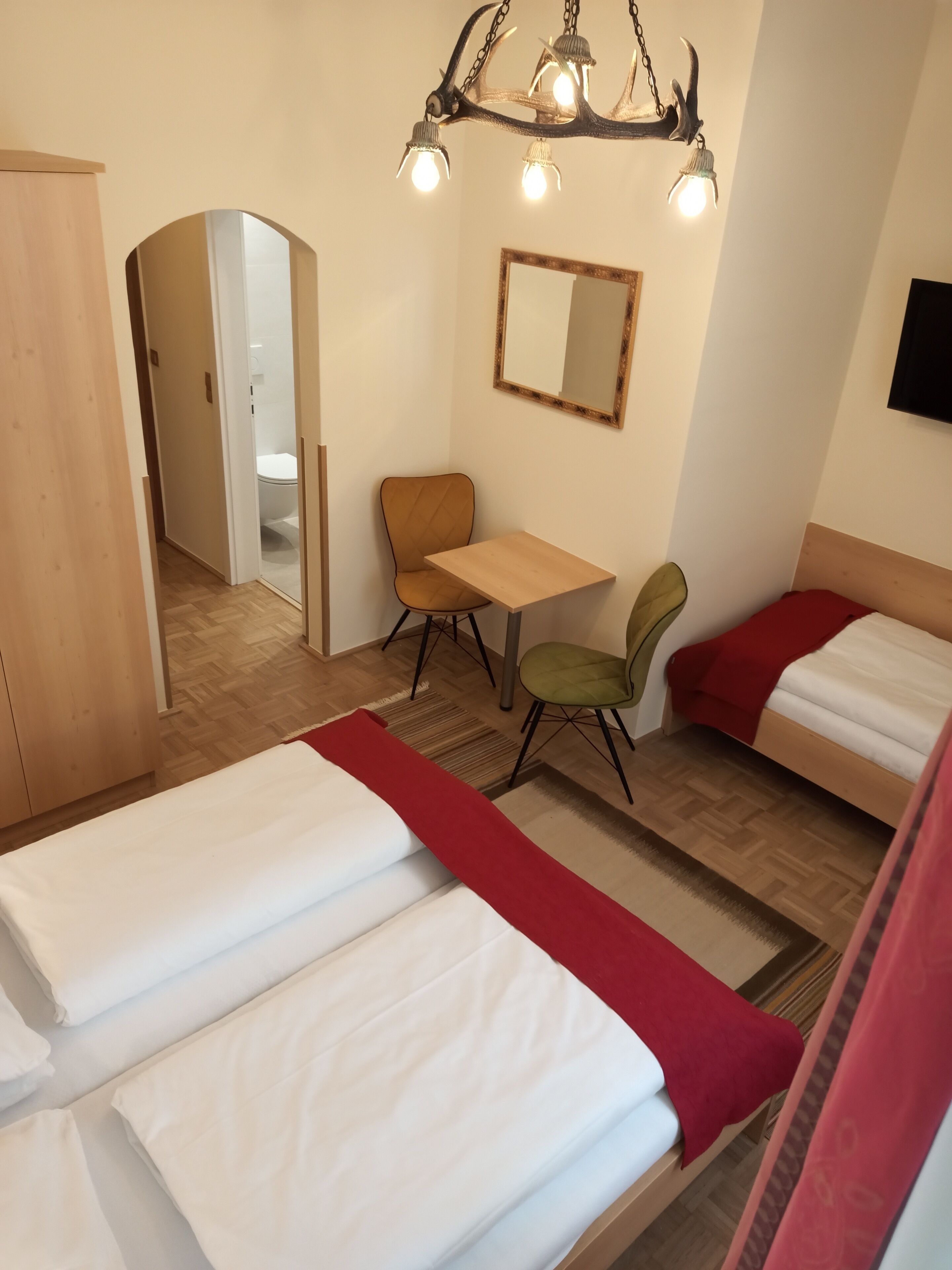 A hotel room with two beds, a wooden desk, a chair, a mirror, and a chandelier.
