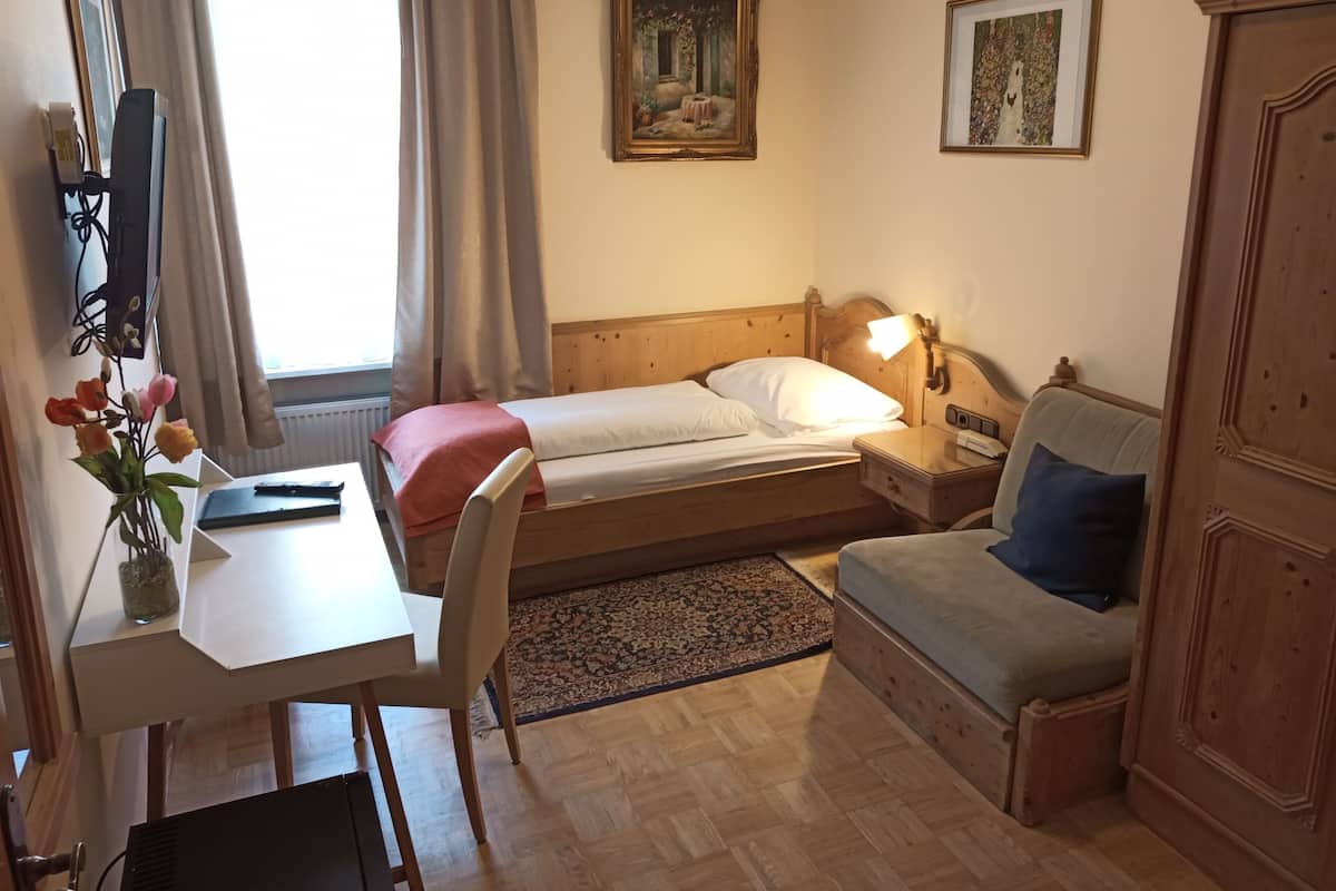 Ein Zimmer mit Bett, Nachttisch, Lampe, Schreibtisch, Stuhl und einer kleinen Couch.