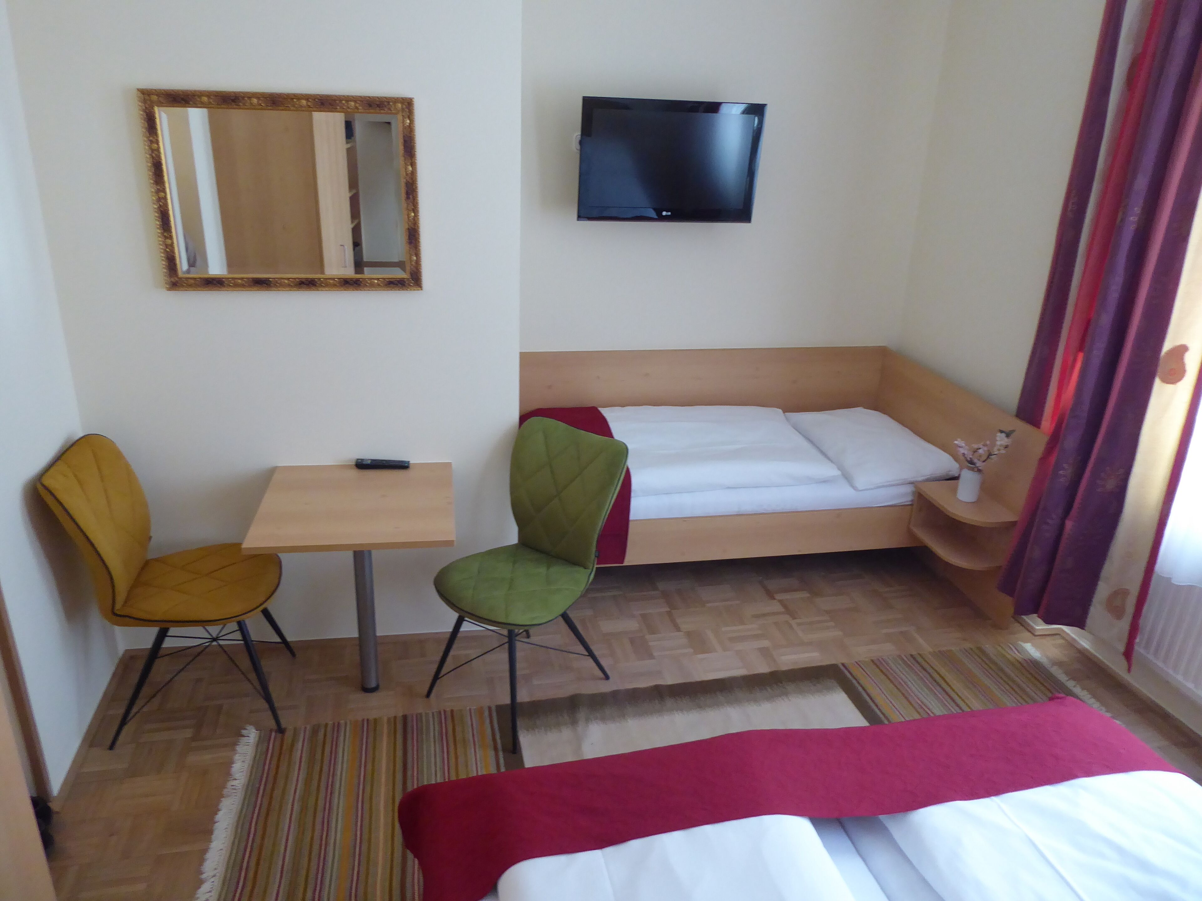 Habitación de hotel con cama, escritorio, dos sillas, televisión y espejo.