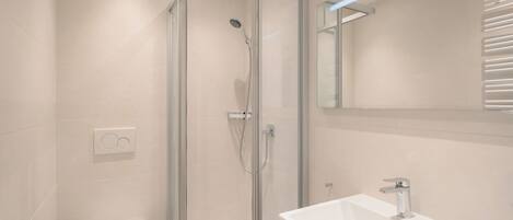 Un baño moderno con ducha envuelta en vidrio, un lavabo blanco y un inodoro.