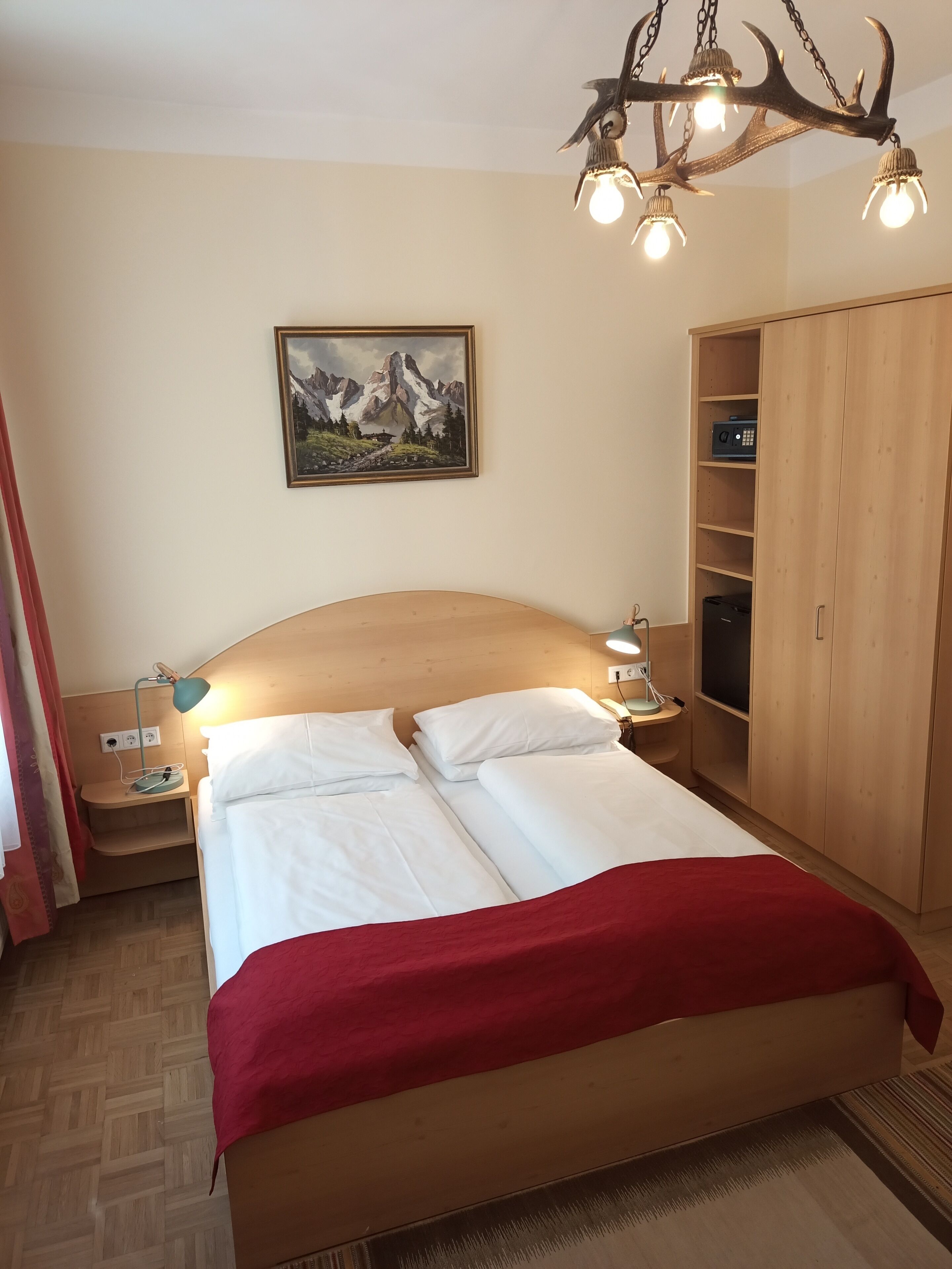 Un dormitorio con una cama grande, un armario de madera, un cuadro de montañas y una araña.