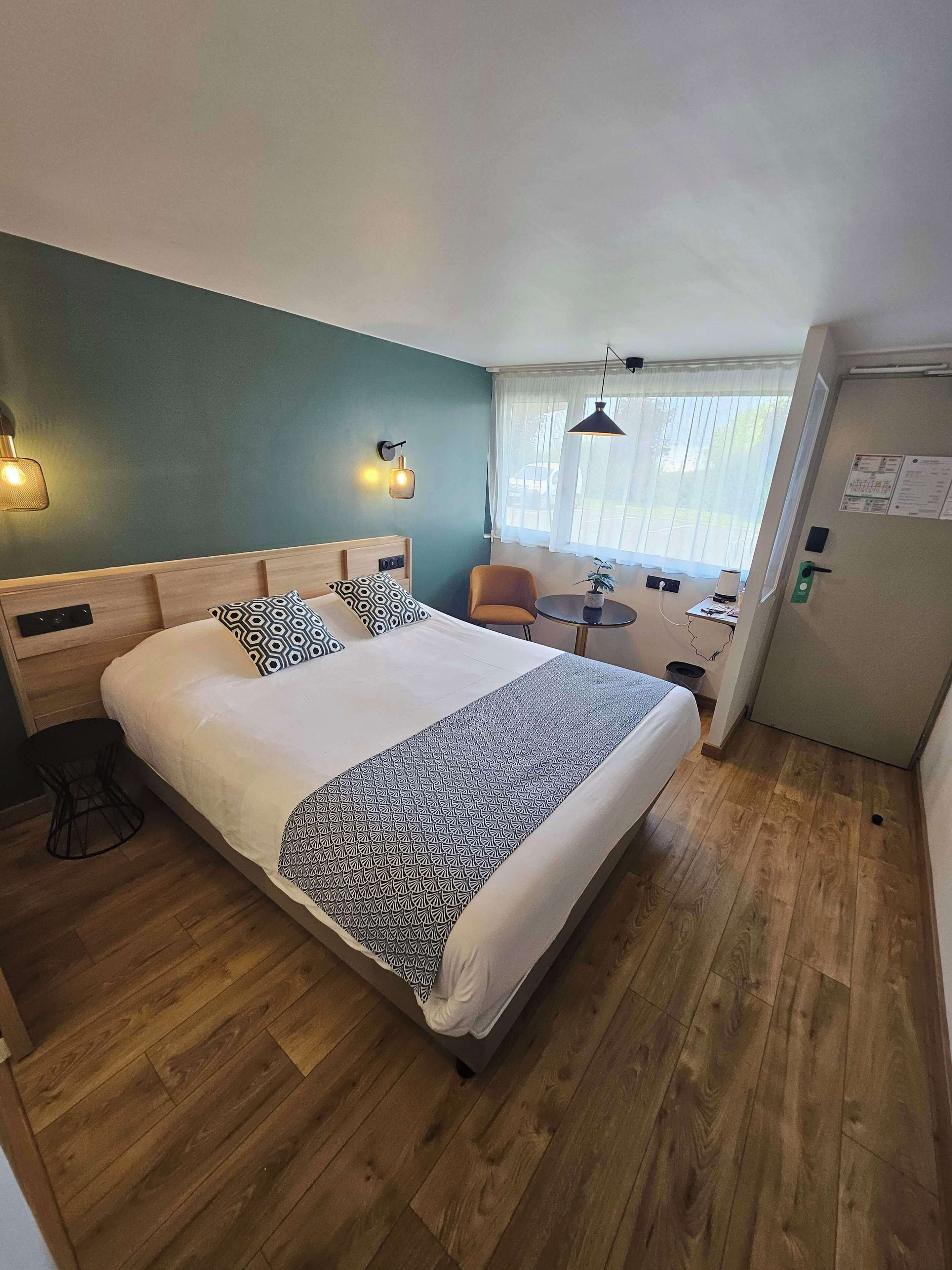 Hotelkamer met een groot bed, een kleine tafel, een stoel en een raam met gordijnen.