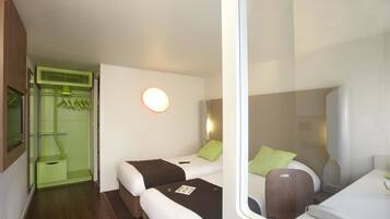 Habitación de hotel con dos camas, un escritorio pequeño, un espejo y un mueble verde con una lámpara.