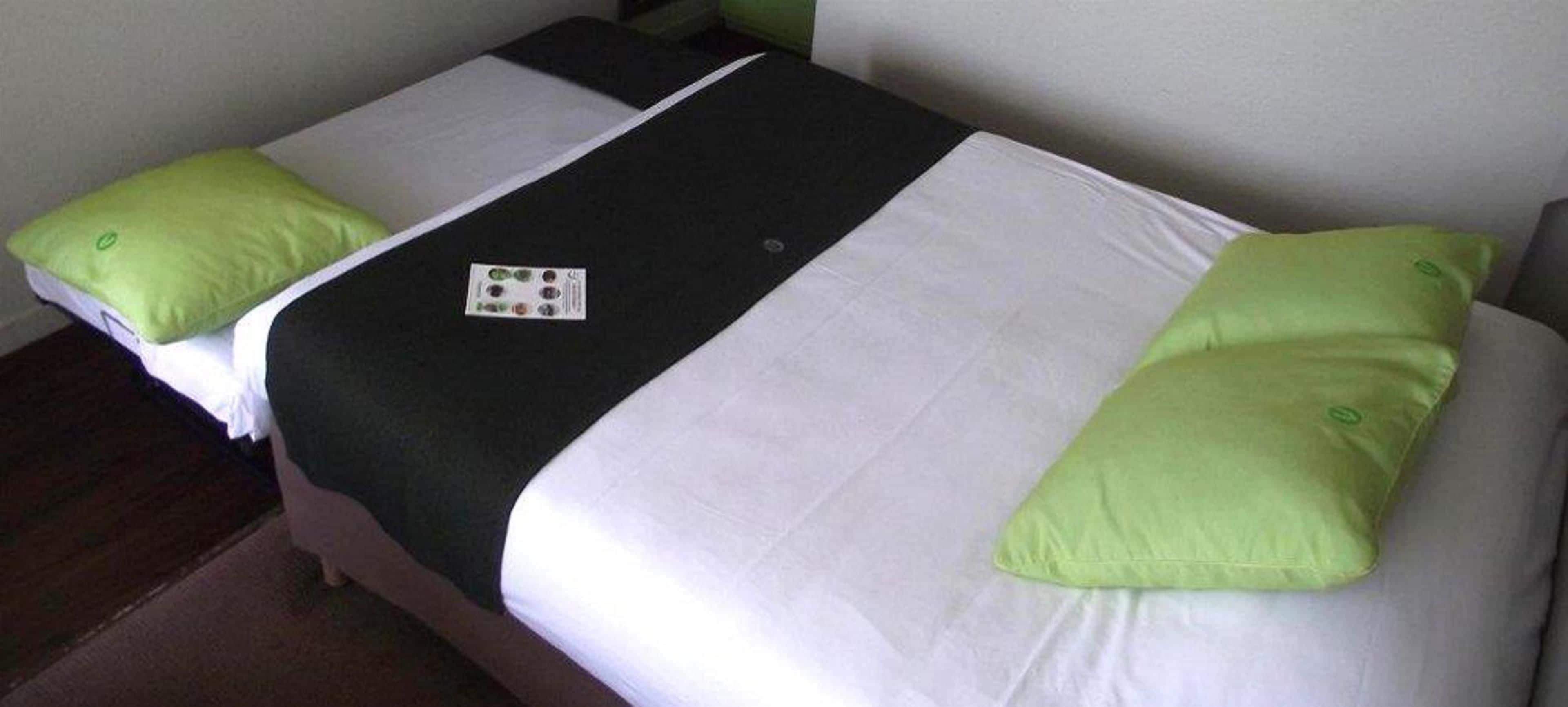 A hotel room with two beds, each with white and green bedding, and a black blanket.