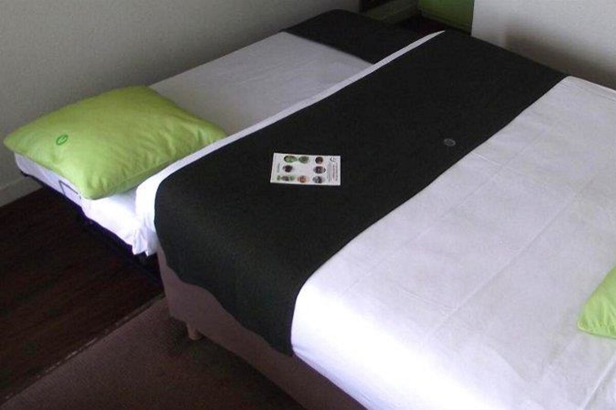 Une chambre d’hôtel avec deux lits, chacun agrémenté de draps blancs et verts, et d’une couverture noire.