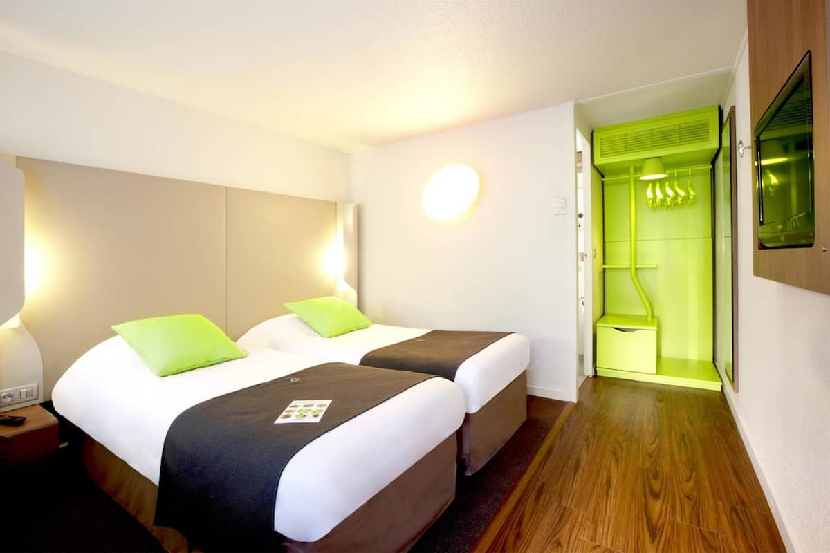 Habitación de hotel con dos camas, una pared verde, un espejo y suelo de madera.