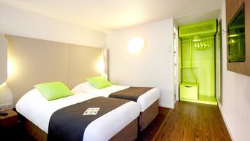 Habitación de hotel con dos camas, una pared verde, un espejo y suelo de madera.