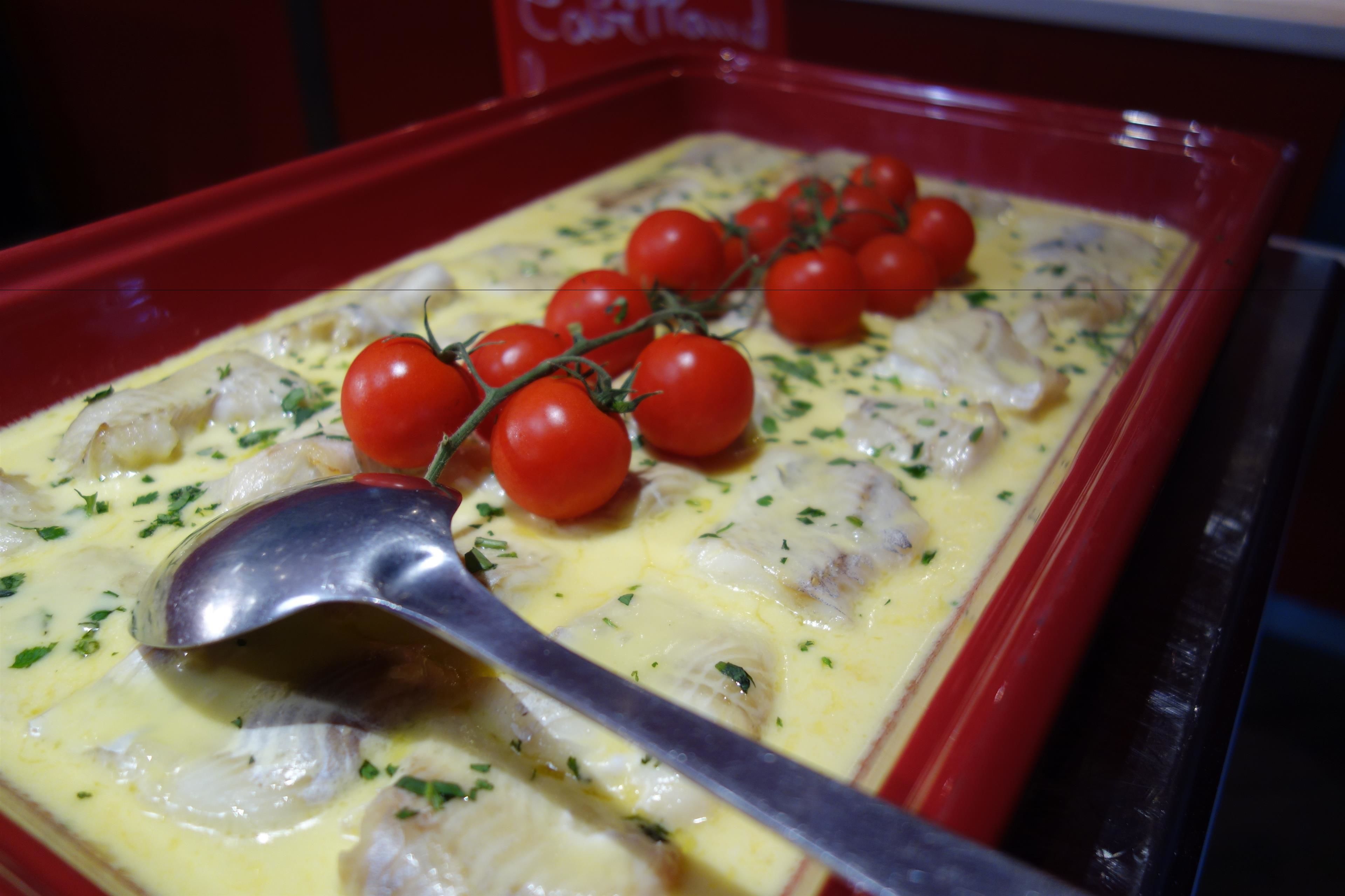 Un plato con pescado, tomates cherry y salsa cremosa en un recipiente para hornear rojo.