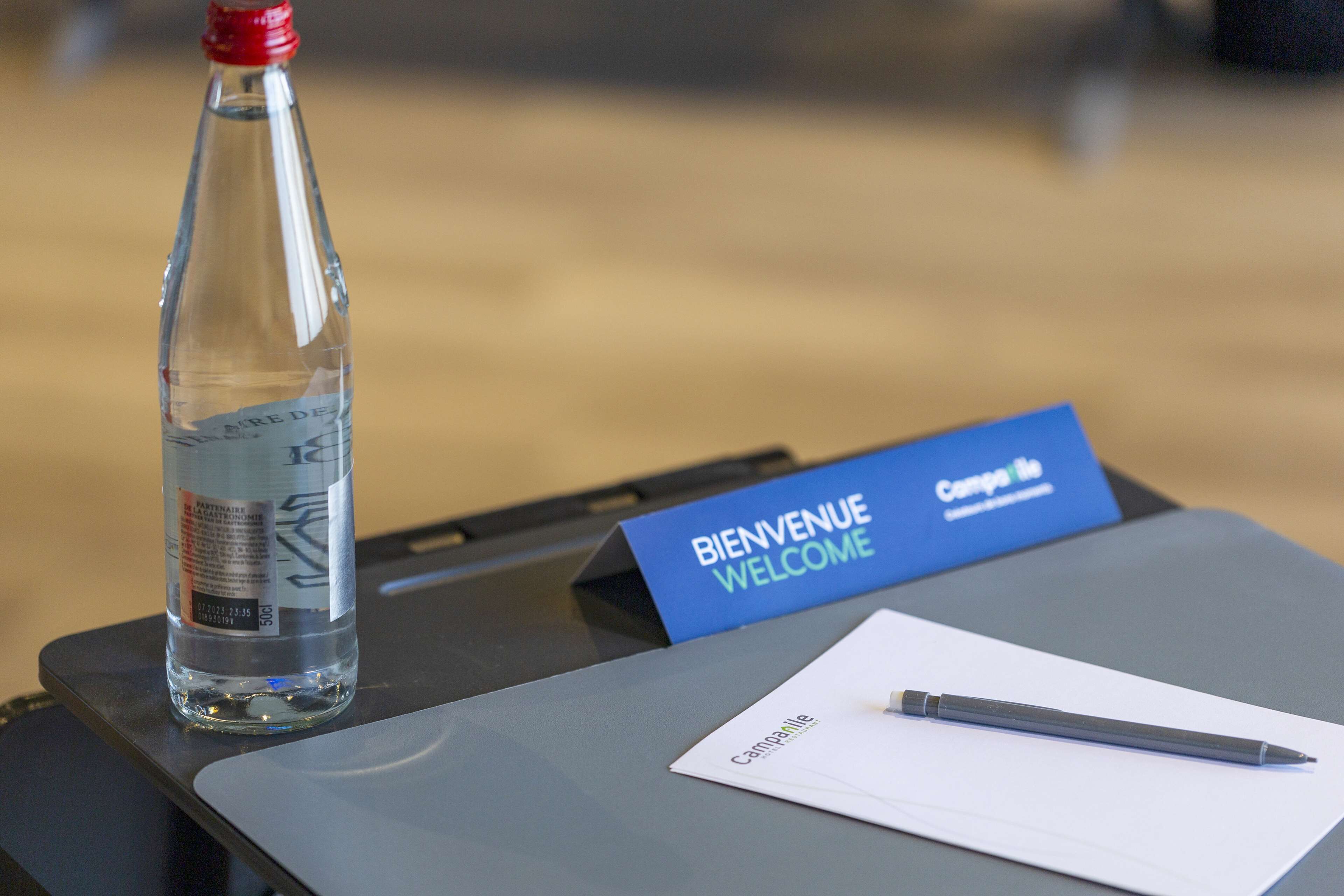 A bottle of water, a welcome sign, and a pen on a table.