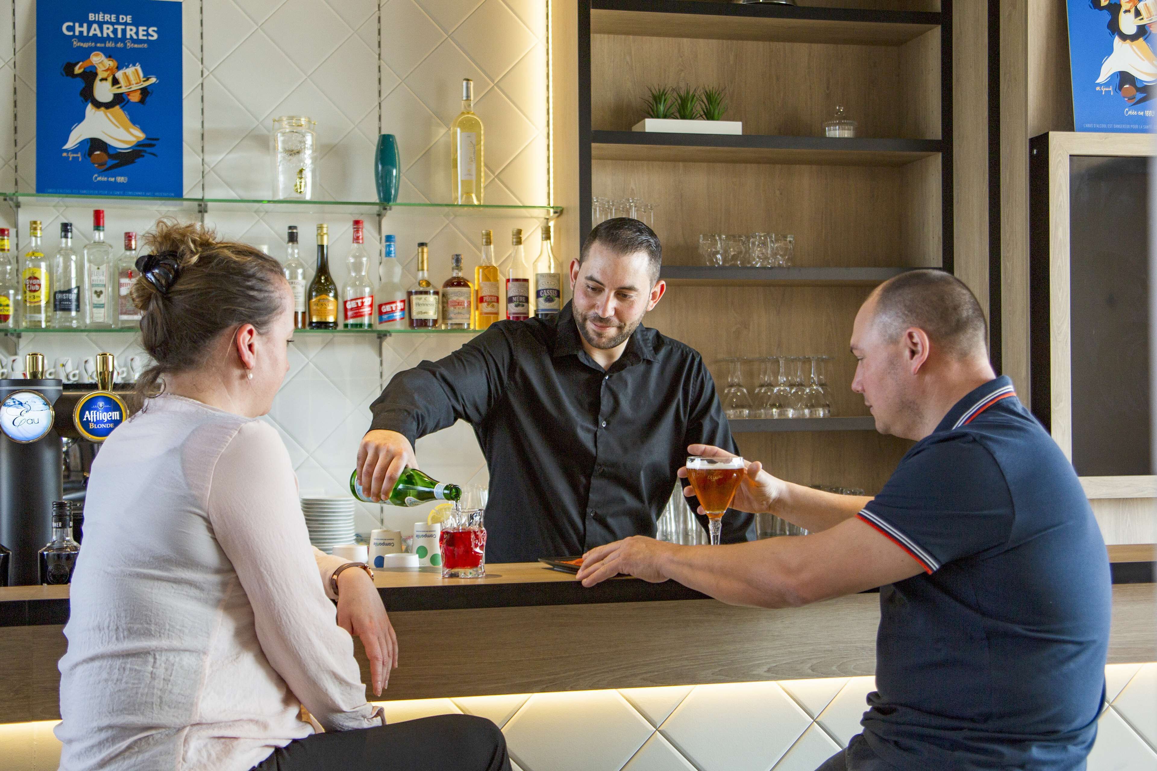 Zona de bar con mostrador, estantes con botellas y vasos.