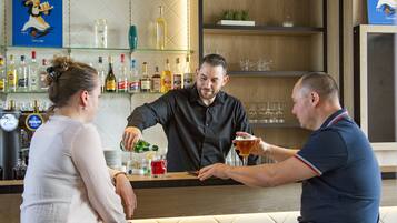 Zona de bar con mostrador, estantes con botellas y vasos.