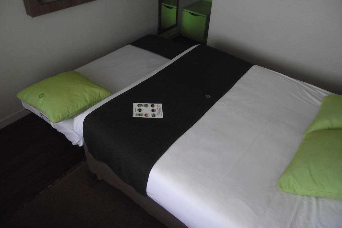 Una cama individual con una colcha blanco y negro, dos almohadas verdes y una tarjeta pequeña sobre la cama.