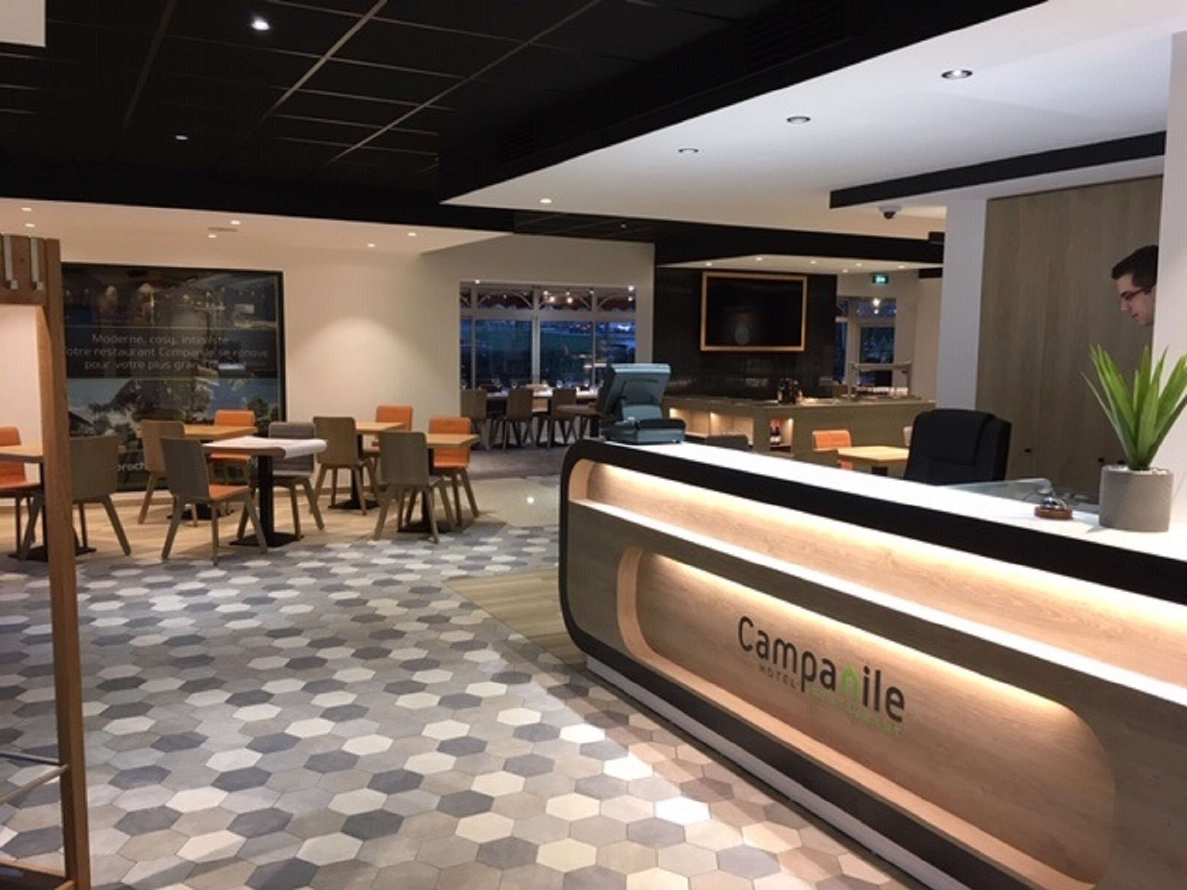A hotel reception area with a modern design, featuring a reception desk labeled "Camparibe," seating arrangements, and a large window offering a view of the cityscape.
