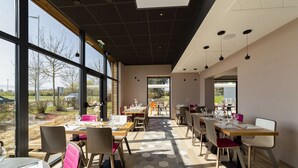 Un restaurante con varias mesas y sillas, amplios ventanales y vistas al exterior.