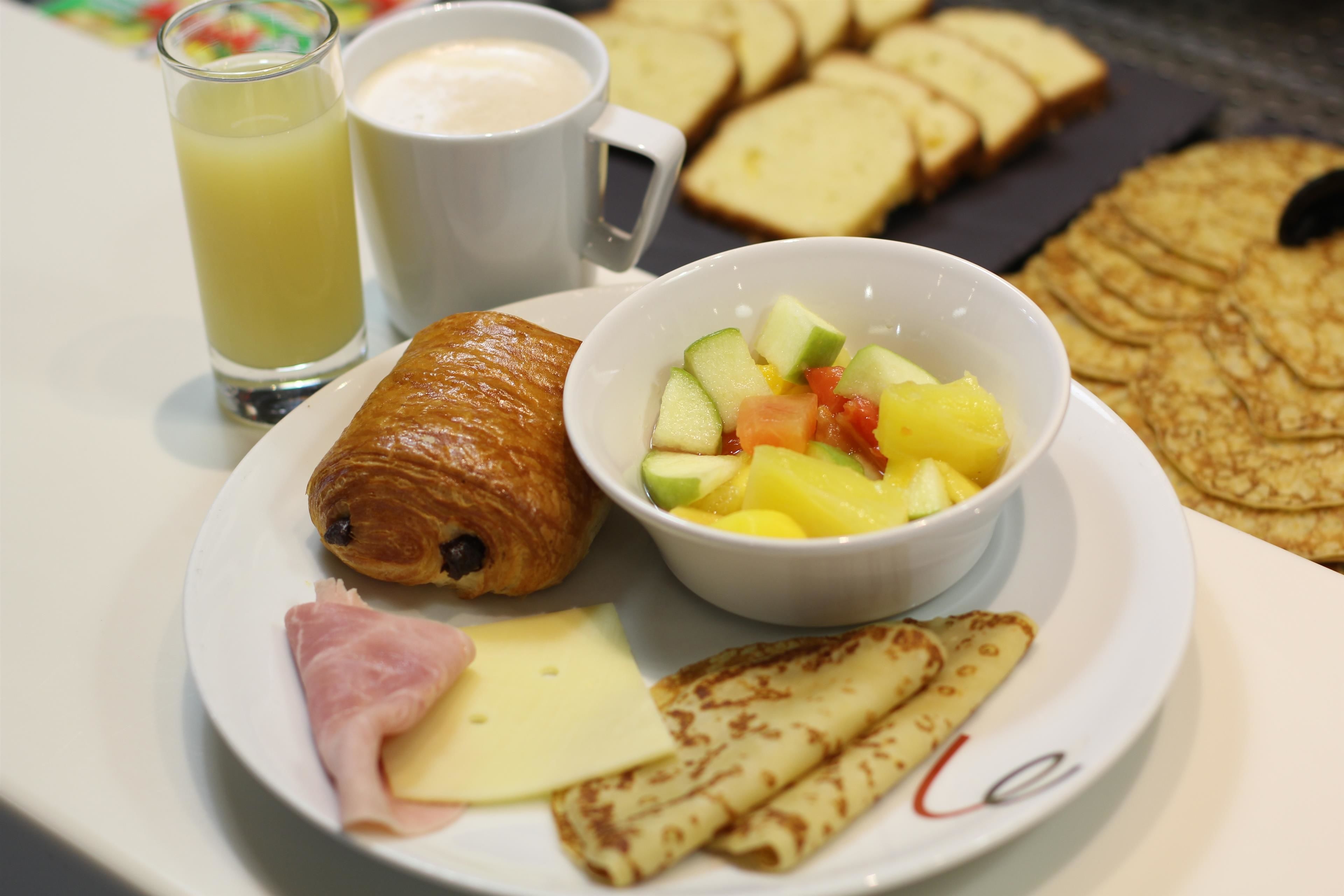 A breakfast plate with croissant, ham, cheese, and crepes, a glass of juice, and a cup of coffee.