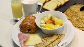 A breakfast plate with croissant, ham, cheese, and crepes, a glass of juice, and a cup of coffee.